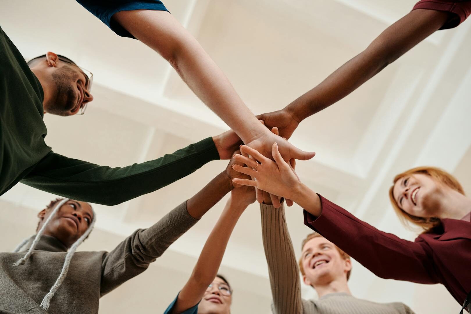 A diverse group of young adults forming a united circle with hands together indoors.